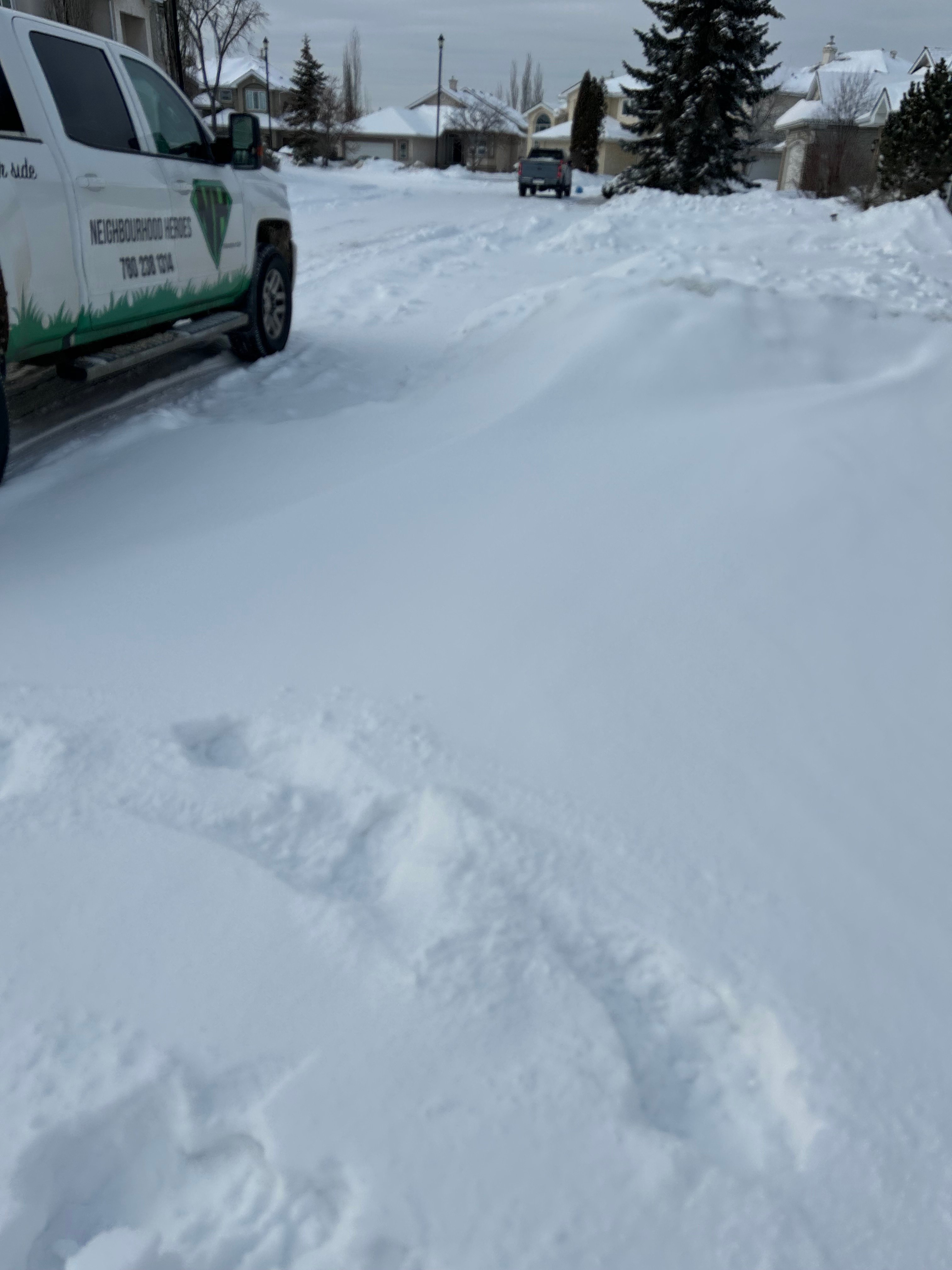 A white Neighbourhood Heroes service truck parked next to a snow-covered residential driveway, ready for Edmonton snow removal.